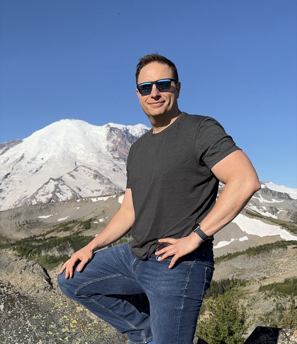 Aaron Holbrook, who lives in Huntley, Illinois and runs Huntley Commons, standing outdoors in front of a snow covered mountain.